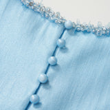Close-up of the Radiance Satin Crop Top by KIKI and JOJO in light blue with a liquid-sheen finish, round buttons, and a hand-beaded pearl neckline embellished with sequins.