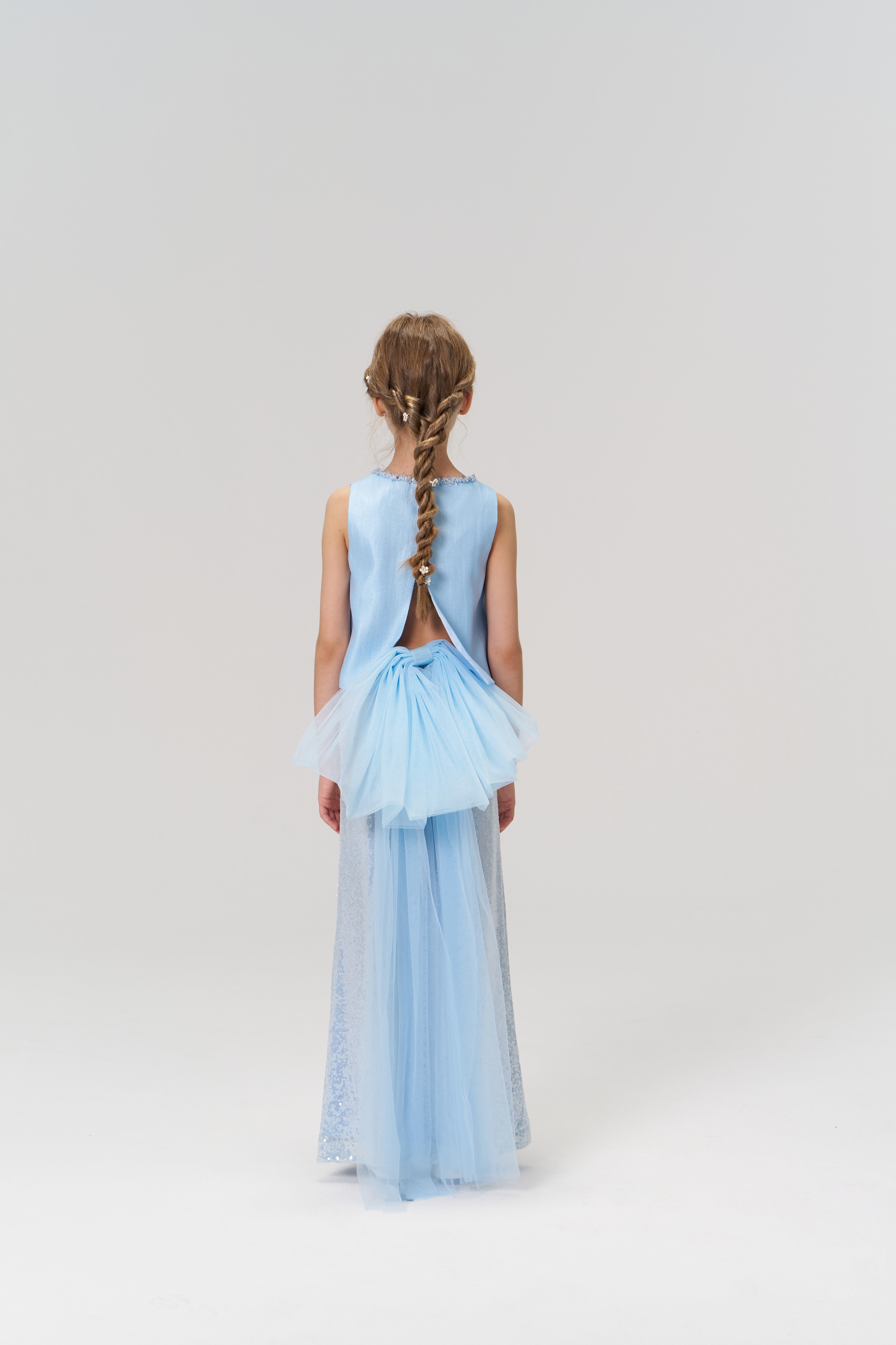 A young girl stands facing away against a plain white background, wearing KIKI and JOJO’s Radiance Sequin Wide-leg Pants.
