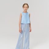 A young girl faces forward, wearing KIKI and JOJO’s Radiance Sequin Wide-leg Pants in light blue with a sleeveless top and white shoes, set against a plain light background.