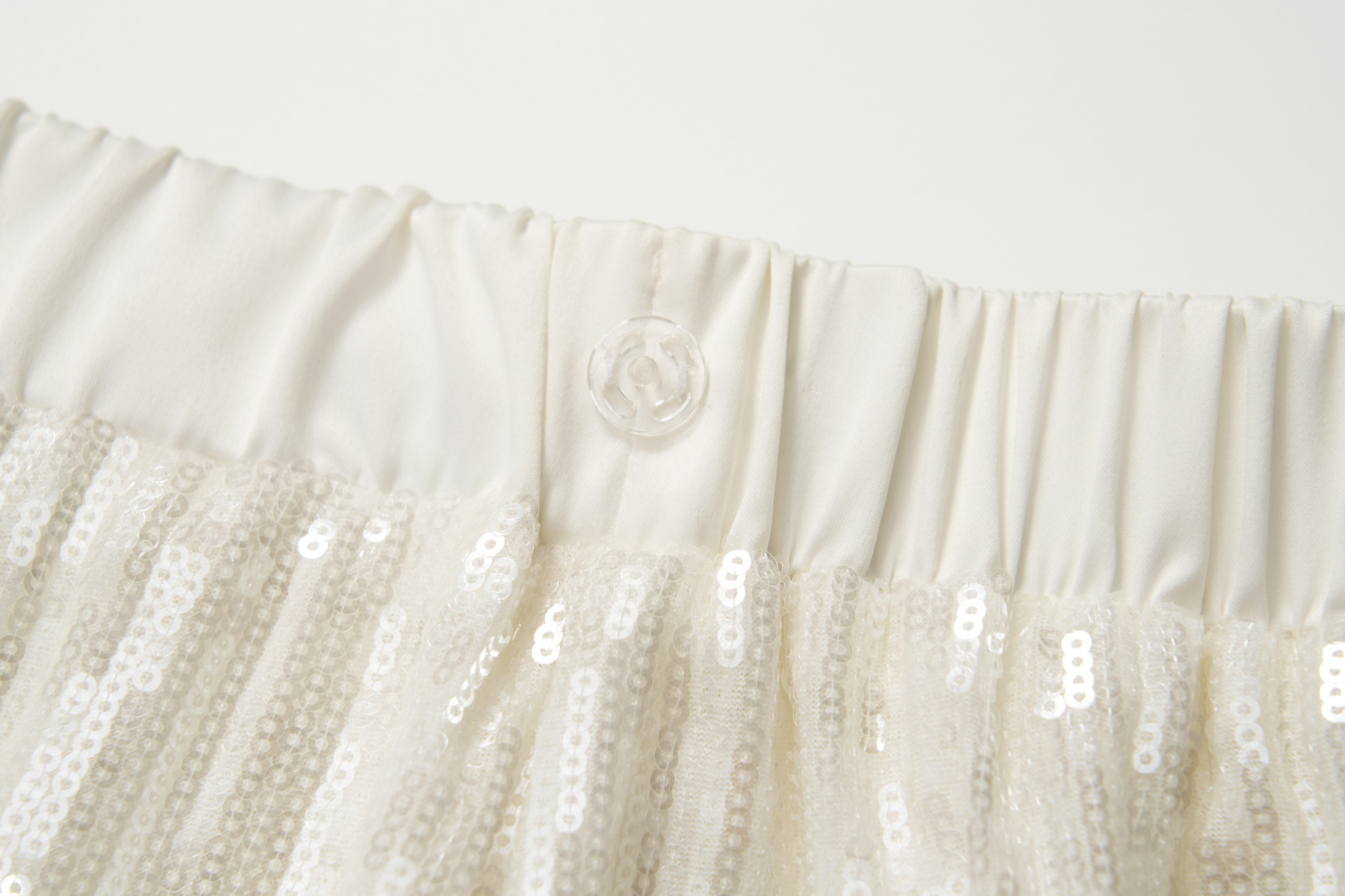 Close-up of an off-white elastic waistband with a transparent button, featured on the KIKI and JOJO Radiance Sequin Wide-Leg Pants with high-rise fit and white sequins.