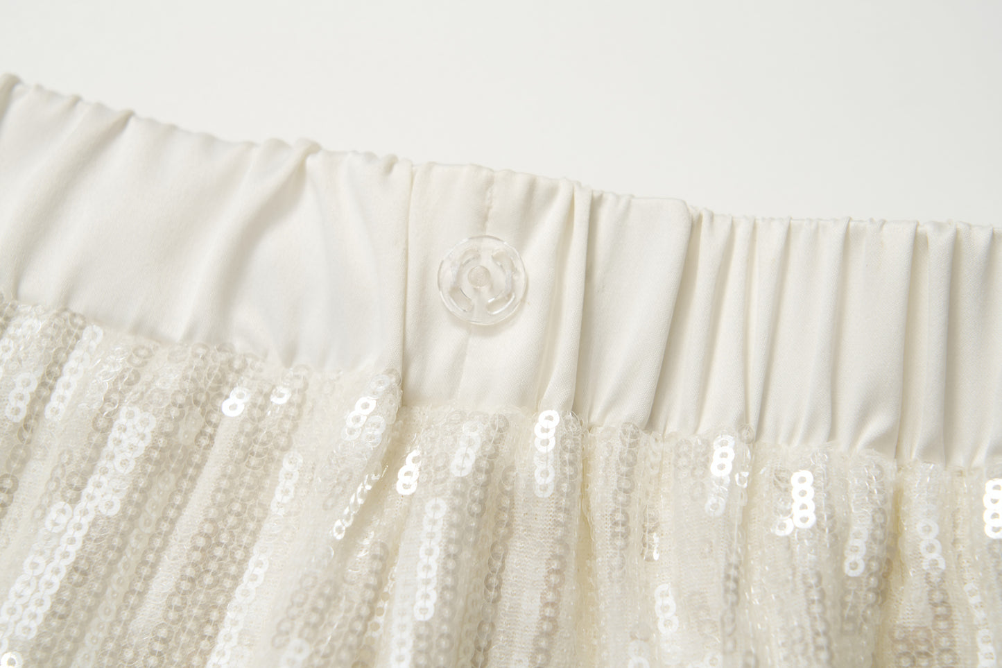 Close-up of an off-white elastic waistband with a transparent button, featured on the KIKI and JOJO Radiance Sequin Wide-Leg Pants with high-rise fit and white sequins.
