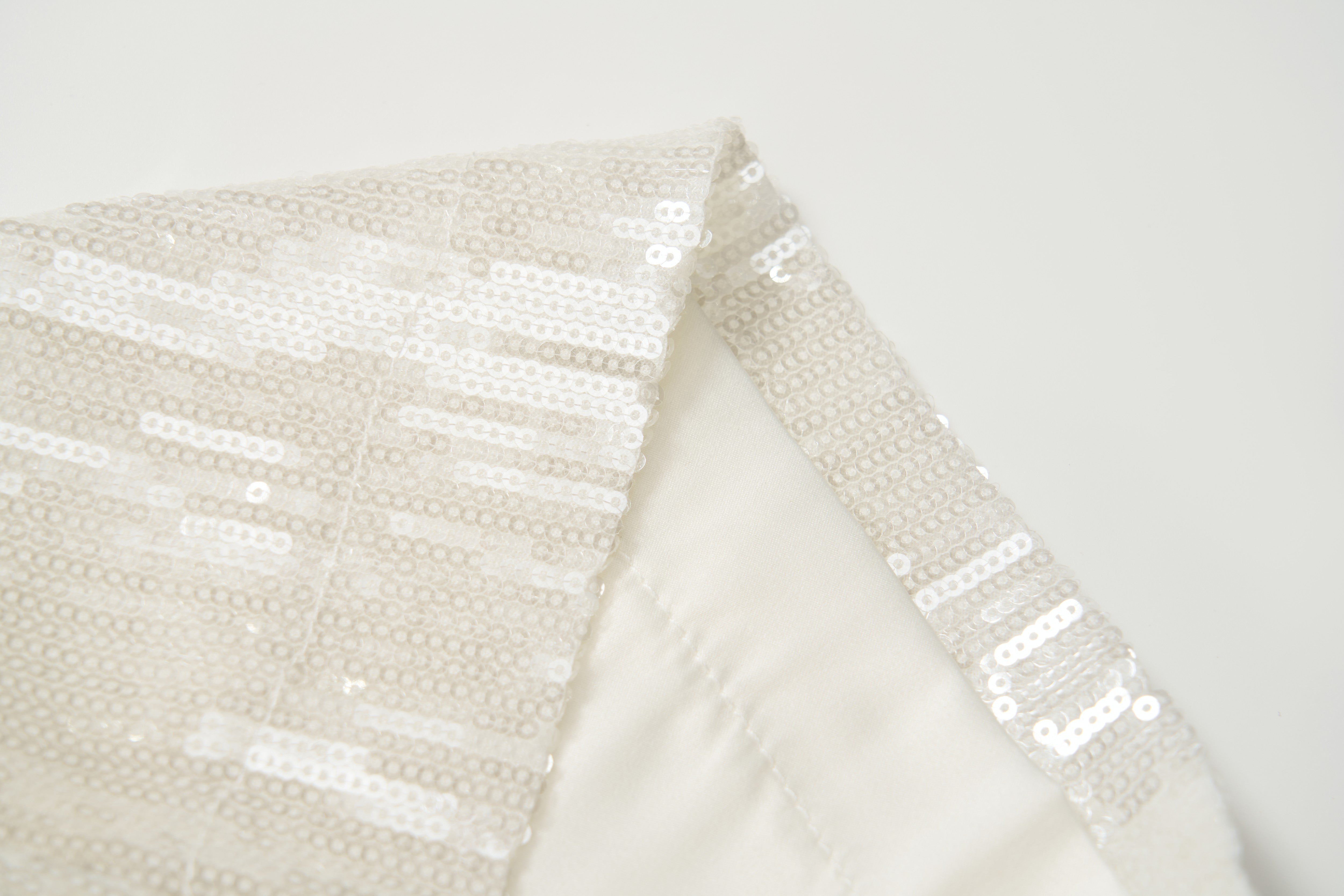 Close-up of Radiance Sequin Wide-Leg Pants by KIKI and JOJO, showcasing shiny sequins stitched in horizontal lines on white fabric against a plain background.