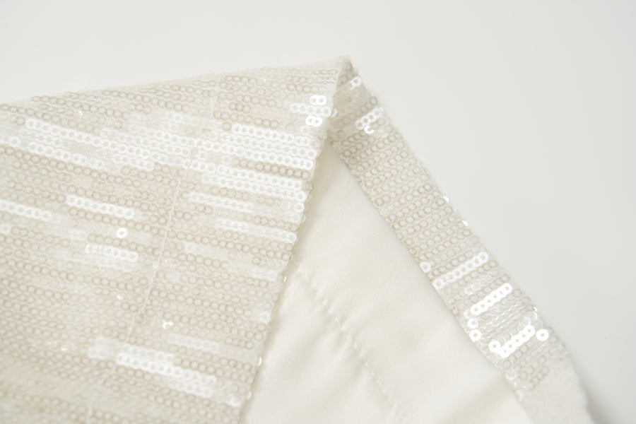 Close-up of Radiance Sequin Wide-Leg Pants by KIKI and JOJO, showcasing shiny sequins stitched in horizontal lines on white fabric against a plain background.