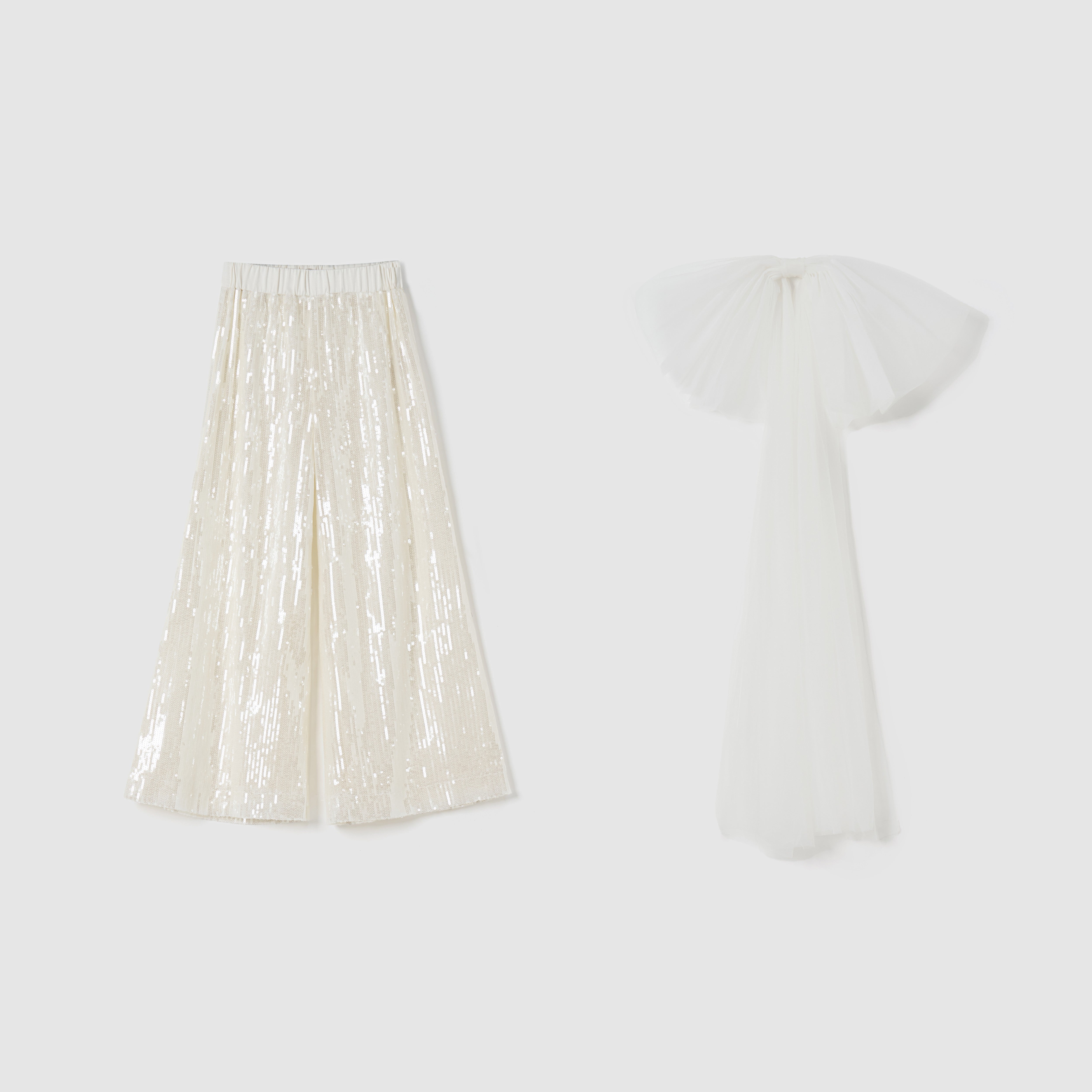 The Radiance Sequin Wide-Leg Pants by KIKI and JOJO, in shiny cream, are displayed beside a long white tulle garment with a detachable bow train on a plain background.