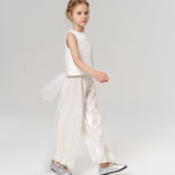 A young girl in a sleeveless white top and KIKI and JOJO Radiance Sequin Wide-Leg Pants with silver shoes walks across a plain light background.