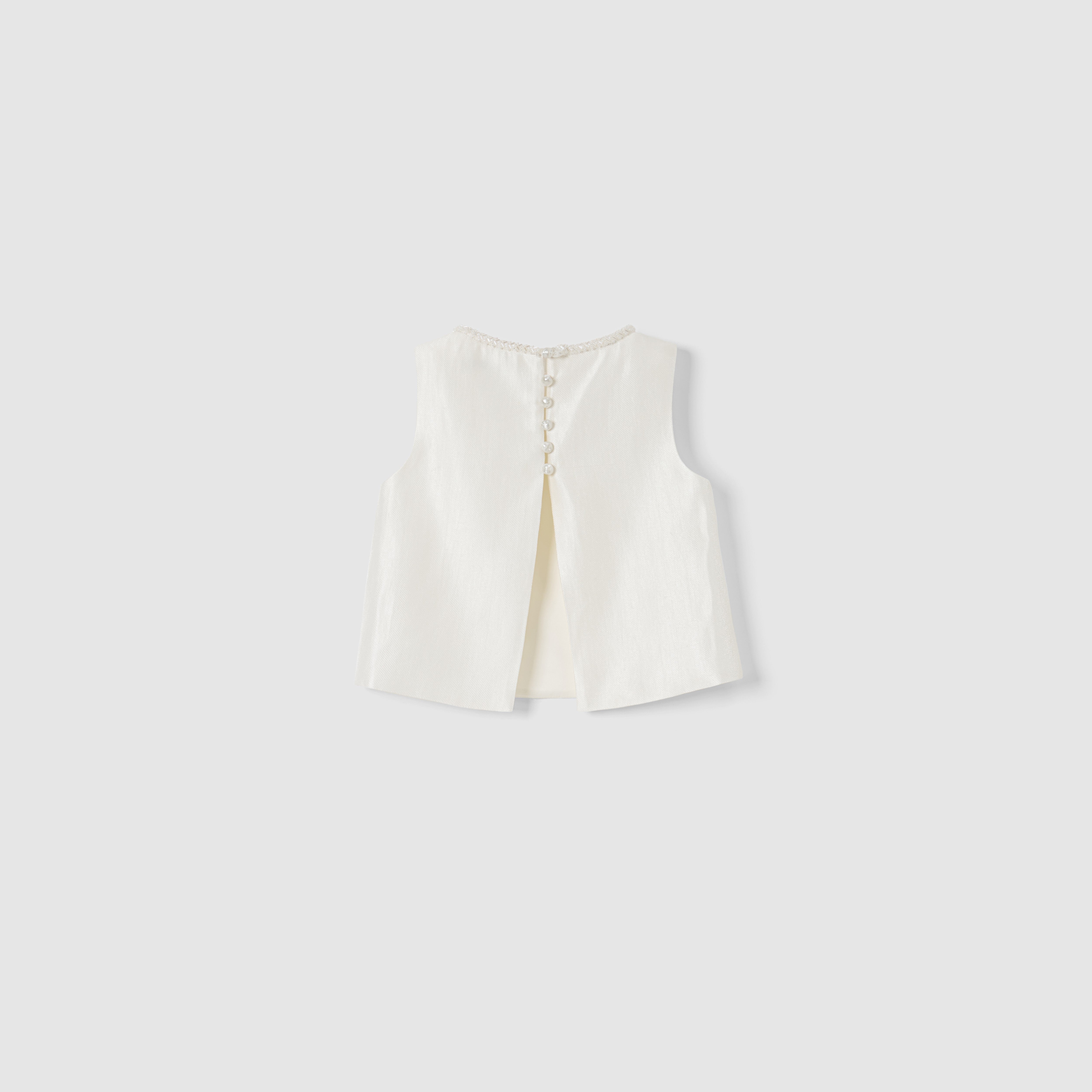 The Radiance Satin Crop Top by KIKI and JOJO is a white sleeveless satin top with a hand-beaded pearl neckline, back slit, and pearl button closures, shown on a plain light grey background.