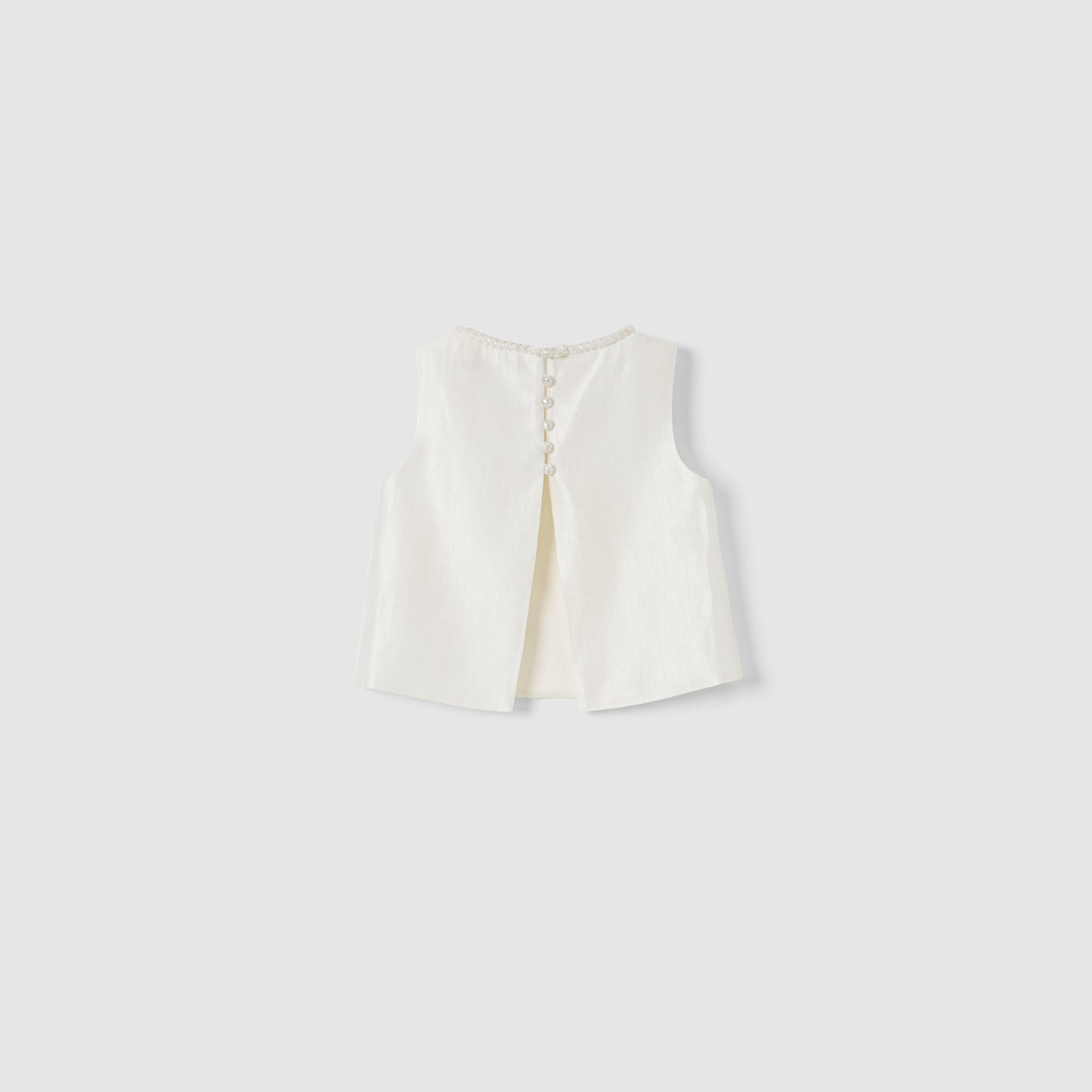 The Radiance Satin Crop Top by KIKI and JOJO is a white sleeveless satin top with a hand-beaded pearl neckline, back slit, and pearl button closures, shown on a plain light grey background.