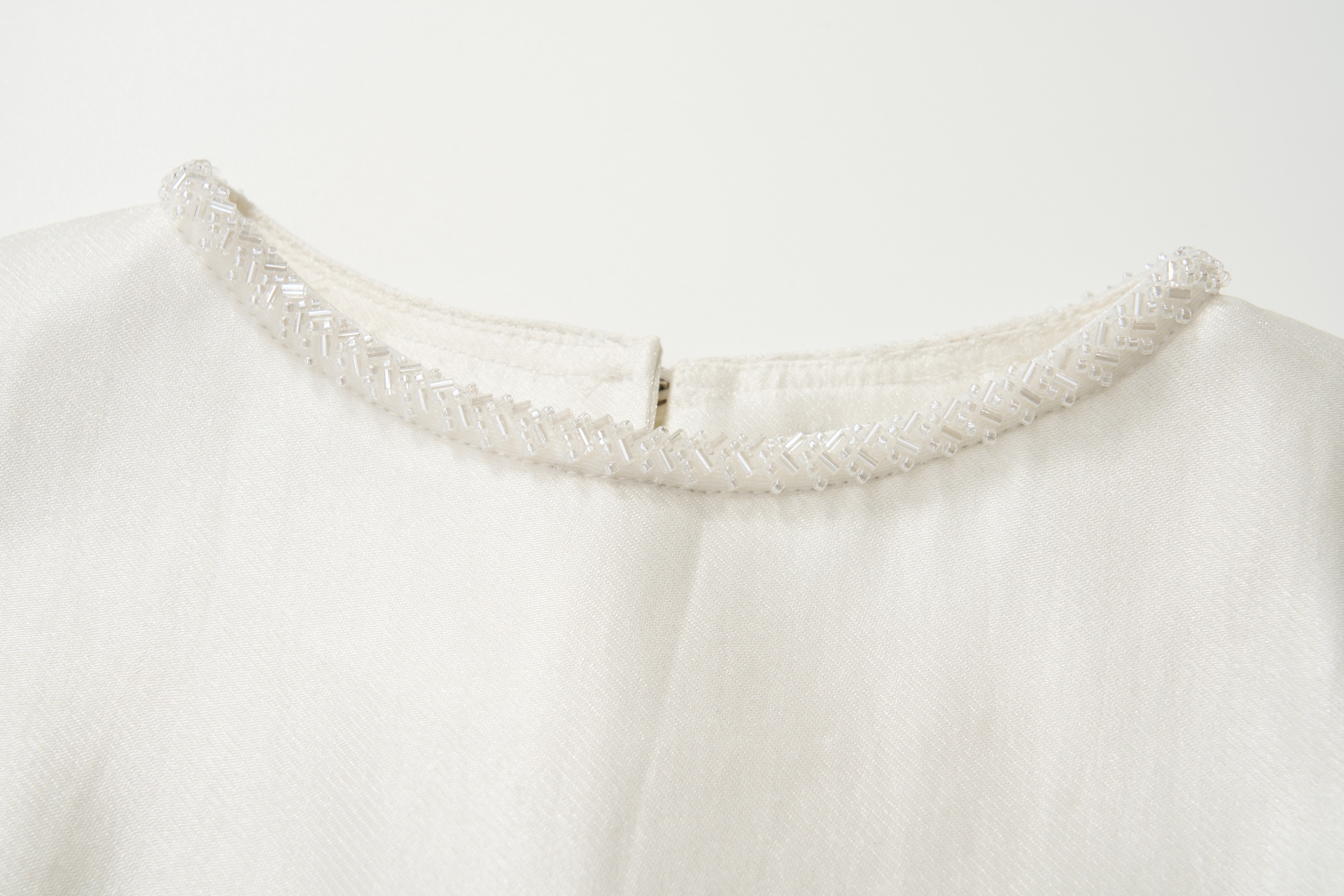 Close-up of the Radiance Satin Crop Top by KIKI and JOJO, showcasing a hand-beaded pearl neckline and small back zipper, displayed on a plain background.