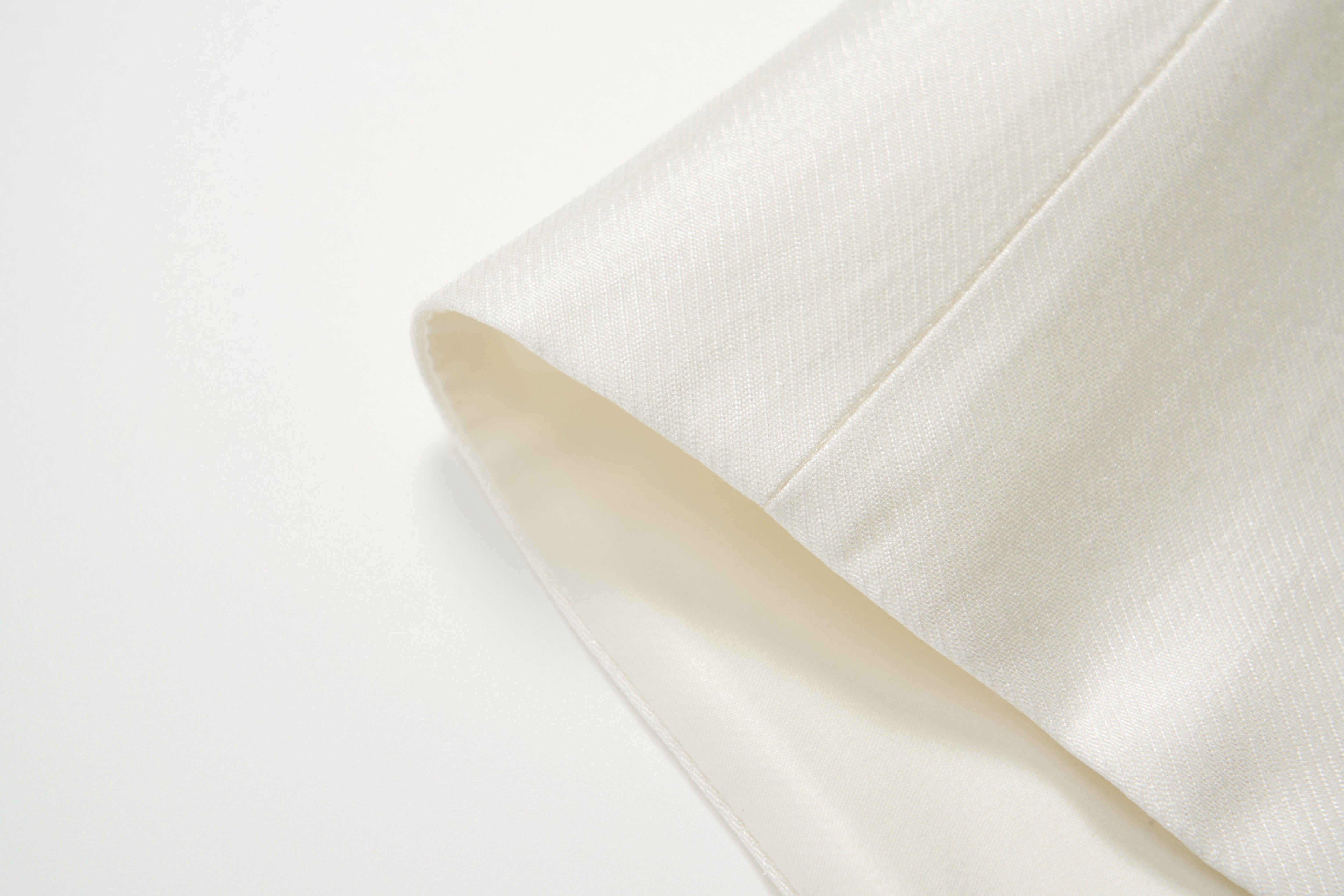 Close-up of the cuff of the cream-colored Radiance Satin Crop Top by KIKI and JOJO, featuring smooth, textured satin fabric and long sleeves, shown against a white background.