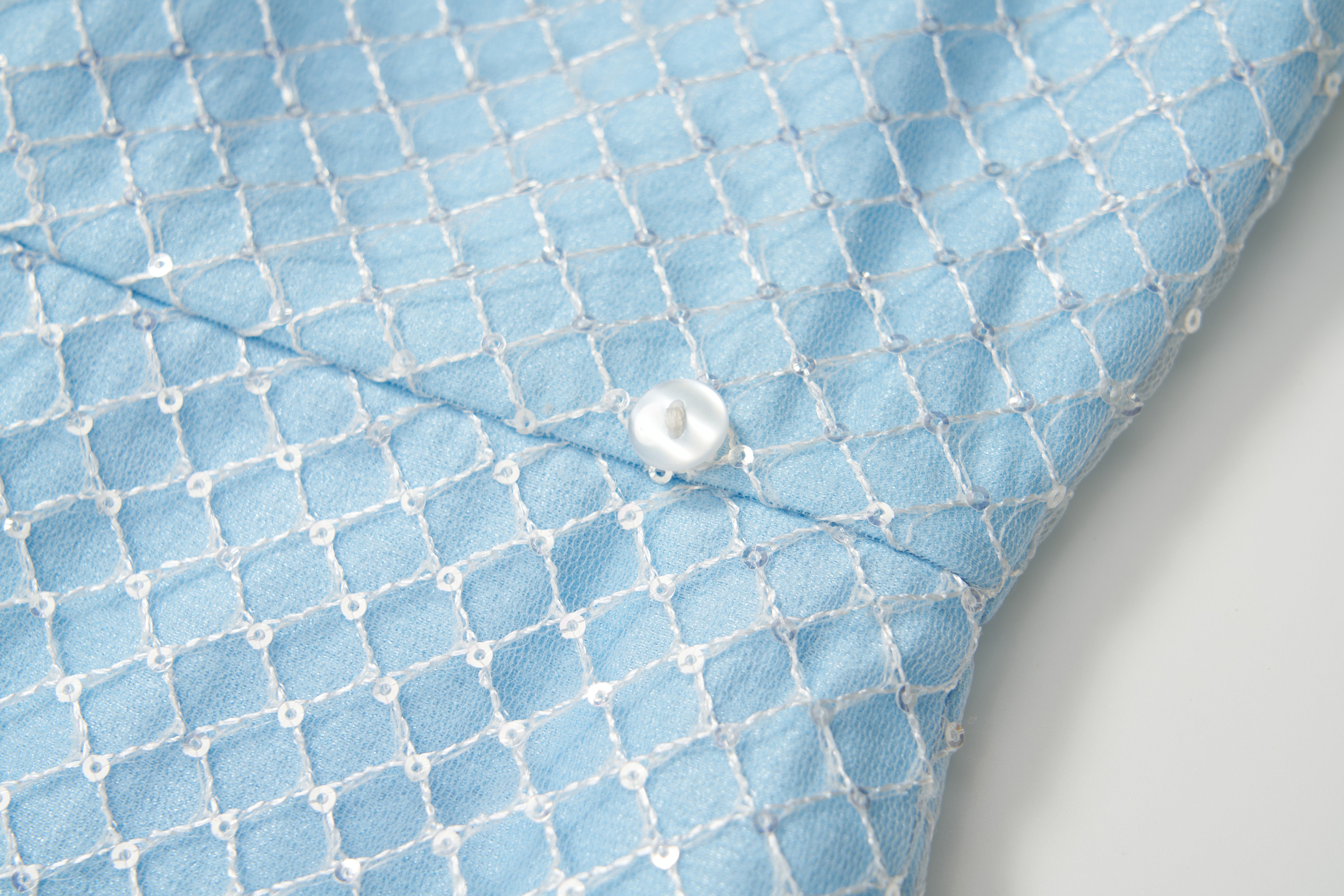 Close-up of the Radiance Sequin Overlay Dress by KIKI and JOJO, featuring light blue fabric with a white lattice pattern and a white button—ideal for convertible dress styles or detachable overskirt designs.