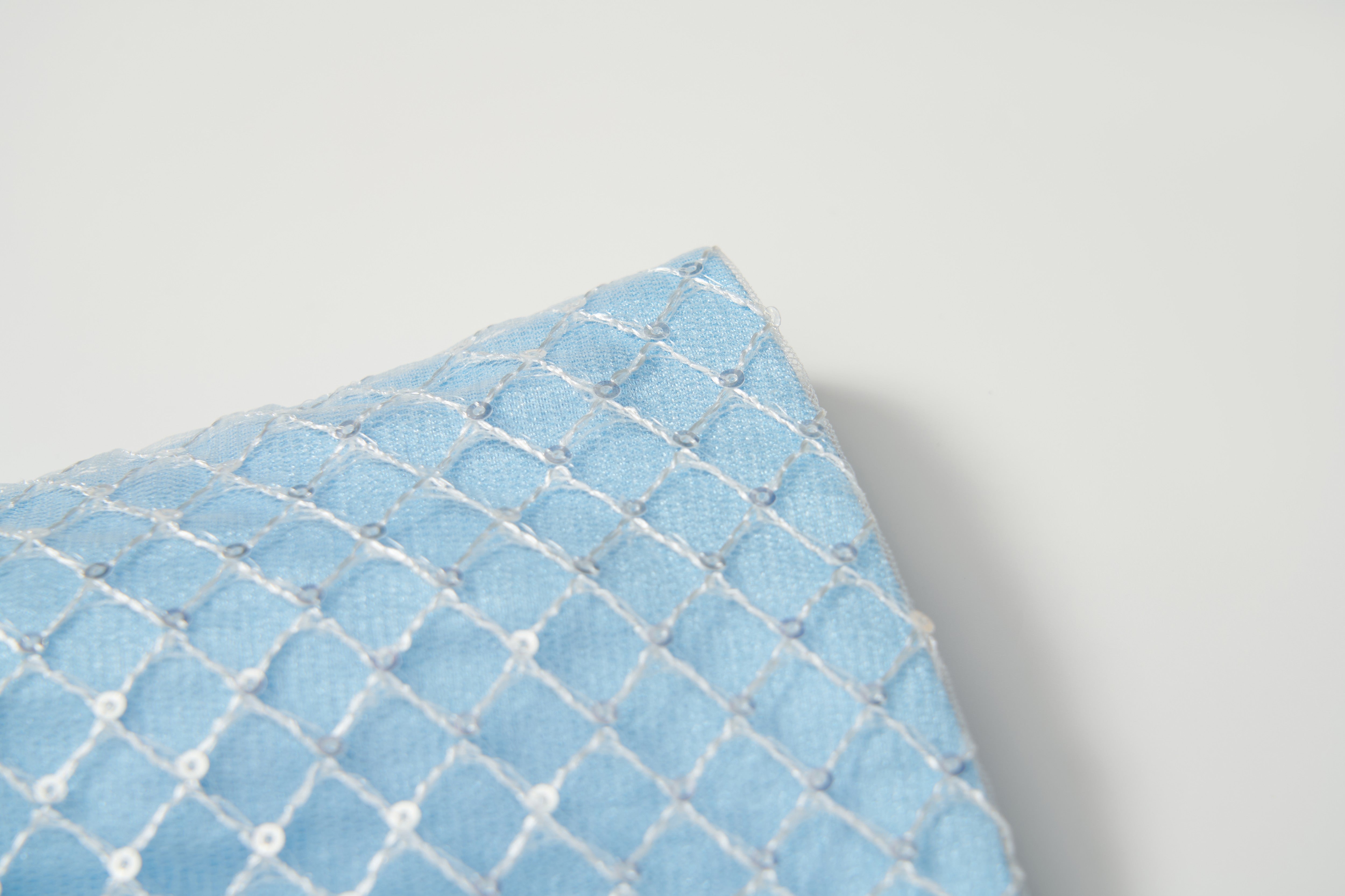 A close-up of the Radiance Sequin Overlay Dress by KIKI and JOJO, with light blue fabric and white diamond-patterned embroidery reminiscent of delicate sequin tulle.