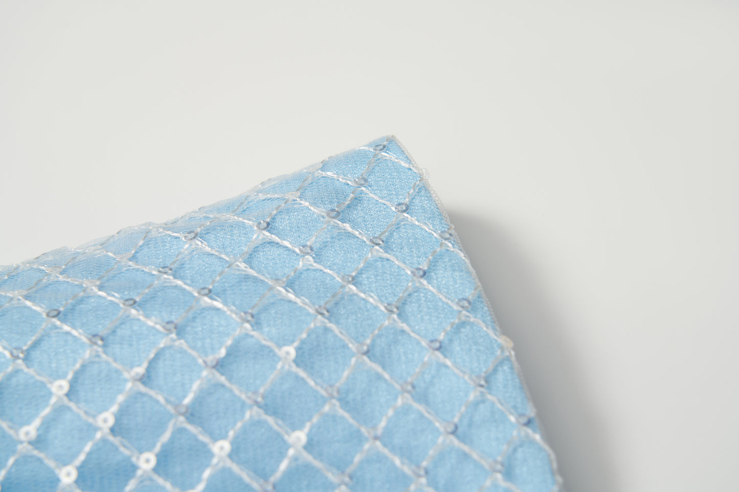 A close-up of the Radiance Sequin Overlay Dress by KIKI and JOJO, with light blue fabric and white diamond-patterned embroidery reminiscent of delicate sequin tulle.