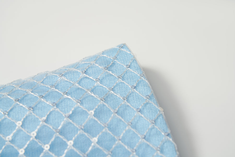 A close-up of the Radiance Sequin Overlay Dress by KIKI and JOJO, with light blue fabric and white diamond-patterned embroidery reminiscent of delicate sequin tulle.
