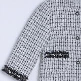 A close-up of the KIKI and JOJO Girls Tweed Jacket in black-and-white checkered tweed, featuring decorative black trim and pearl accents on the sleeves and pockets.