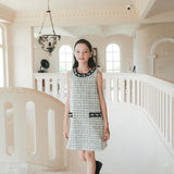 A girl in the KIKI and JOJO Girls Tweed Dress – Black & White Checkered Pearl stands on a marble staircase with arched windows behind her, capturing a timeless moment of luxury fashion.