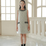 A girl stands indoors on a marble floor, wearing the KIKI and JOJO Girls Tweed Dress – Black & White Checkered Pearl, paired with black socks and shoes, exuding timeless luxury fashion.