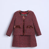 The KIKI and JOJO Girls Tweed Jacket – Burgundy Velvet Pearl is a two-piece set with a velvet-trimmed burgundy jacket, elegant brooch, and matching skirt, shown against a plain light background.