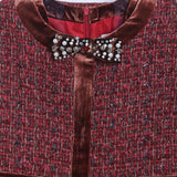A close-up of the KIKI and JOJO Girls Tweed Jacket – Burgundy Velvet Pearl, featuring textured burgundy tweed, brown velvet trim, a pearl bow brooch at the collar, and two front pockets.