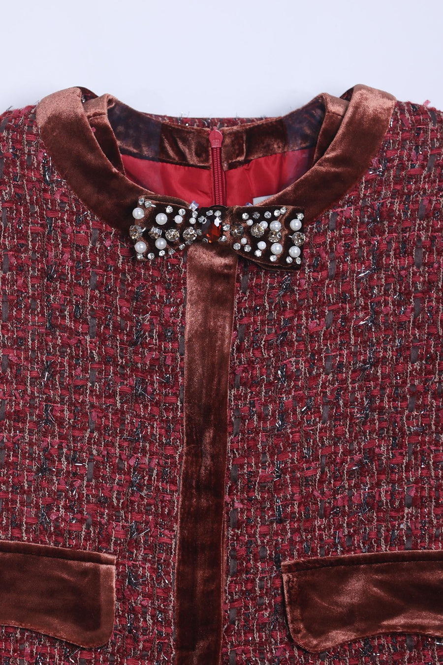 A close-up of the KIKI and JOJO Girls Tweed Jacket – Burgundy Velvet Pearl, featuring textured burgundy tweed, brown velvet trim, a pearl bow brooch at the collar, and two front pockets.