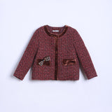 The KIKI and JOJO Girls Tweed Jacket – Burgundy Velvet Pearl features a red patterned tweed, brown velvet trim, long sleeves, two front pockets, and a small bow on the left pocket, shown on a white background.