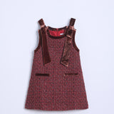 The KIKI and JOJO Girls Handmade Tweed Dress – Burgundy Velvet Bow features textured burgundy fabric, velvet shoulder straps, two front pockets, and detachable velvet bows, shown laid flat on a light background.