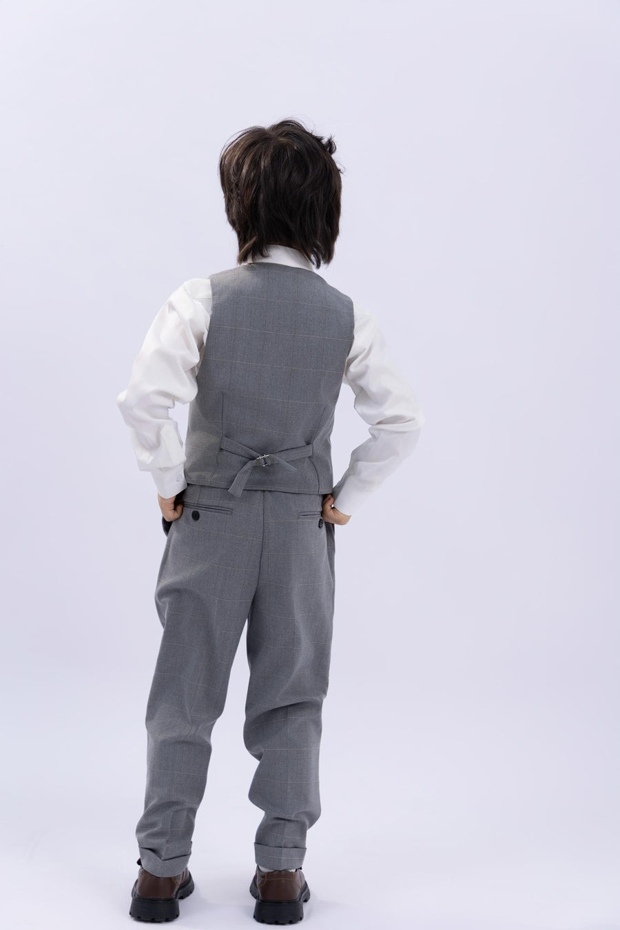 A child wearing the KIKI and JOJO Kids Suit Jacket in light gray checkered, wrinkle-free fabric (ages 3-14), stands with hands on hips, back to camera, against a plain light background.