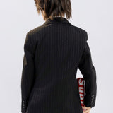 A child in KIKI and JOJO Kids Suit Pants – Black (3-14 Years), classic fit and wrinkle-free, stands with their back to the camera, holding a red object labeled "Supreme" behind them.