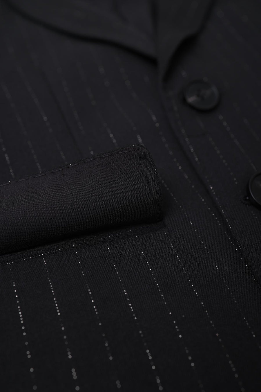 Close-up of the KIKI and JOJO Kids Suit Jacket – Black (3-14 Years), classic fit with subtle vertical pinstripes, a pocket, two buttons, and wrinkle-free fabric.