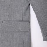 A close-up of the KIKI and JOJO Kids Suit Jacket in gray, classic fit, wrinkle-free, shows the herringbone pocket with flap, sleeve, and side seam against a white background. For ages 3-14 years.