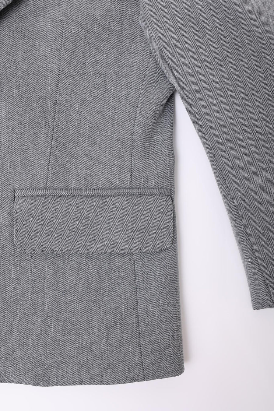 A close-up of the KIKI and JOJO Kids Suit Jacket in gray, classic fit, wrinkle-free, shows the herringbone pocket with flap, sleeve, and side seam against a white background. For ages 3-14 years.