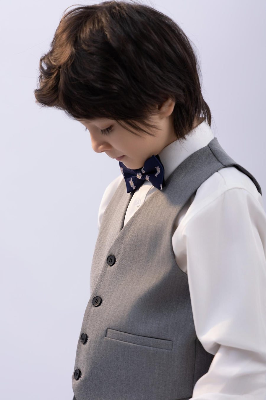 A young boy models the KIKI and JOJO Kids Suit – Gray 3-Piece Set (3-14 Years), classic fit and wrinkle-free, paired with a white shirt and patterned bow tie against a simple light background.