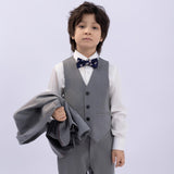 A young boy wears the KIKI and JOJO Kids Suit Jacket – Gray (3-14 Years), Classic Fit, Wrinkle-Free, and holds a matching jacket against a plain light background.