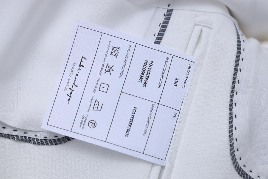 Close-up of the KIKI and JOJO Kids Suit Jacket – White (3-14 Years), Classic Fit, wrinkle-free, with a label showing care instructions, material details, and a signature for a timeless look.