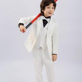 A young boy wears a KIKI and JOJO Kids Suit Vest – White (3-14 Years), classic fit and wrinkle-free, paired with black shoes, standing with a red baseball bat over his shoulder against a plain light background.
