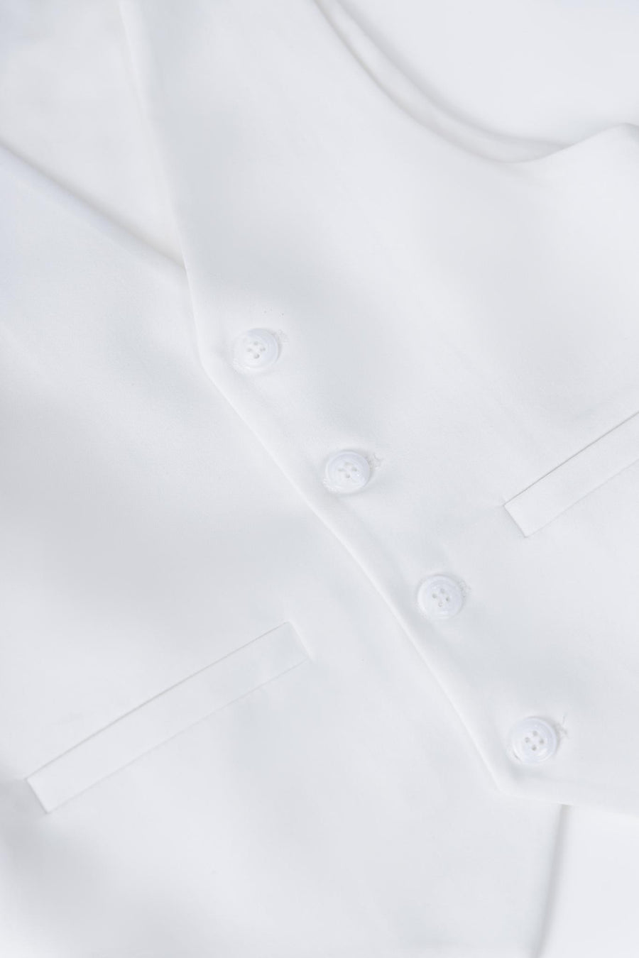Close-up of the KIKI and JOJO Kids Suit Vest – White (3-14 Years), Classic Fit and wrinkle-free, featuring four buttons and two slit pockets, laid flat on a white surface.