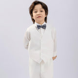 A young boy stands against a plain background, hands behind his back, dressed in a KIKI and JOJO Kids Suit Vest – White (3-14 Years), a classic fit and wrinkle-free design, paired with a white shirt and gray bow tie.