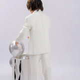 A child wearing the KIKI and JOJO Kids Suit Vest – White (Classic Fit, Wrinkle-Free, 3-14 Years) stands with their back to the camera, reaching into a white bag of silver balloons against a plain background.