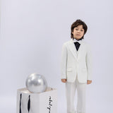 A young boy in a KIKI and JOJO Kids Suit Vest – White (3-14 Years), classic fit and wrinkle-free, stands beside a large white shopping bag with black handles, topped with a metallic silver balloon.