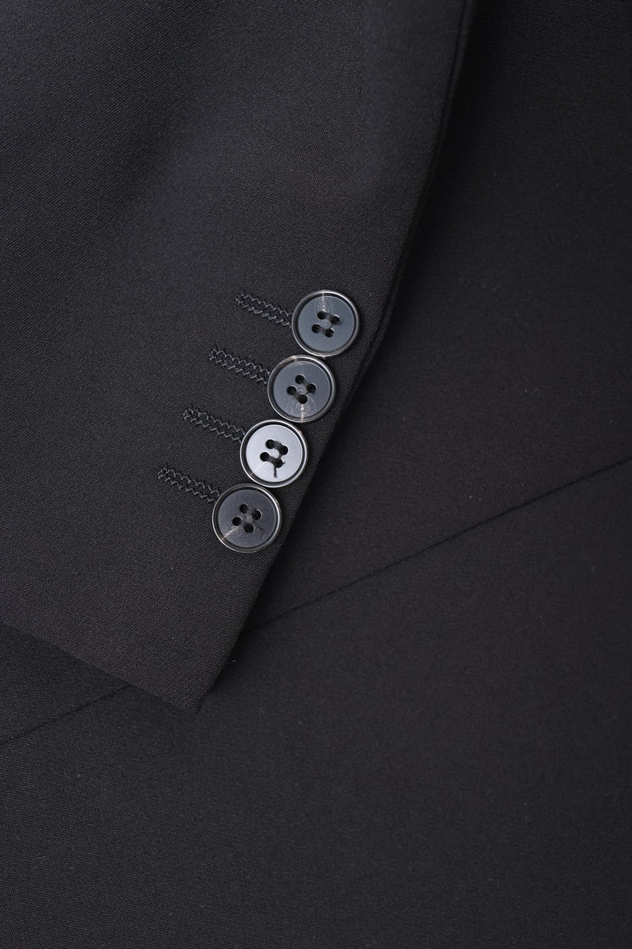 Close-up of the KIKI and JOJO Kids Suit Jacket – Black (3-14 Years), featuring four black buttons on the cuff. This slim-fit, wrinkle-free jacket is displayed against a matching black background.