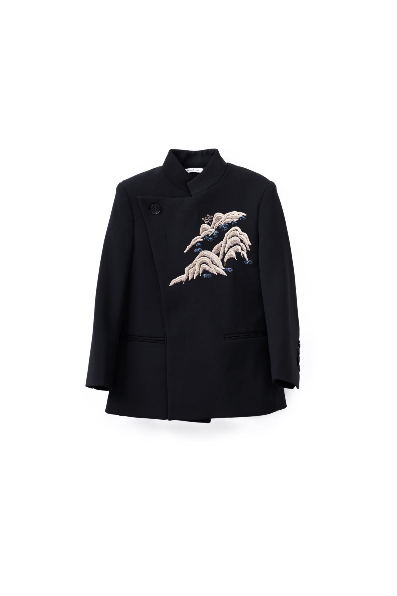 The KIKI and JOJO Kids Suit Jacket in black (ages 3-14) is a slim-fit, wrinkle-free blazer with a classic Mandarin collar and an asymmetrical front featuring wave-like embroidery on the left chest.