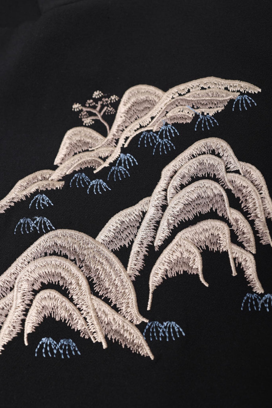The KIKI and JOJO Kids Suit Jacket – Black (3-14 Years) features beige embroidered hills with blue accents and a small tree on wrinkle-free fabric; a stylish, slim-fit option for kids.