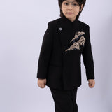 A young child with medium-length dark hair and glasses wears the KIKI and JOJO Kids Suit Jacket in black (3-14 years), a slim-fit, wrinkle-free style, standing against a plain light background.