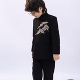 A young boy wears the KIKI and JOJO Kids Suit Jacket in black (slim-fit, wrinkle free), featuring embroidered detail and a classic Mandarin collar, as he stands looking down next to a red balloon on a white background.