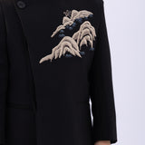 A child wearing the KIKI and JOJO Kids Suit Jacket – Black (Slim-Fit, Wrinkle Free, 3-14 Years) with a classic Mandarin collar and embroidered mountain detail, stands against a plain light background.
