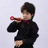 A young boy wears the KIKI and JOJO Kids Dress Shirt – Black Long Sleeve (Classic Fit, 3-14 Years) with a red bow tie, holding a red toy microphone against a plain light background.