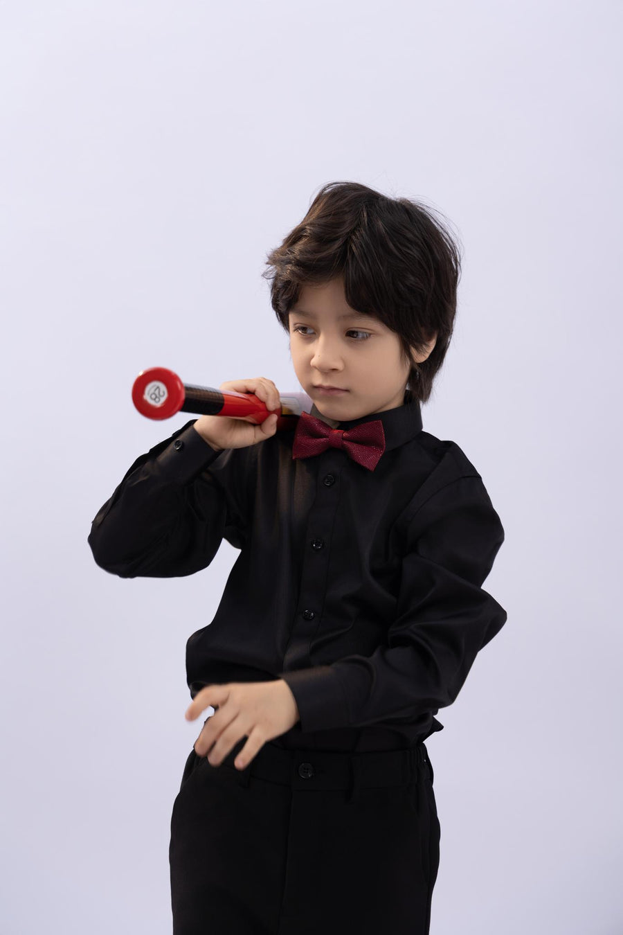 A young boy wears the KIKI and JOJO Kids Dress Shirt – Black Long Sleeve (Classic Fit, 3-14 Years) with a red bow tie, holding a red toy microphone against a plain light background.