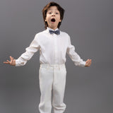A young boy in a white KIKI and JOJO Kids Dress Shirt – White Long Sleeve (3-14 Years) – Classic Fit stands with arms open and mouth wide, highlighting this classic formal shirt style against a plain gray background.