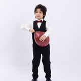 A young boy in a formal suit wears the KIKI and JOJO Kids Bow Tie – Burgundy Bear, a pre-tied adjustable satin bow tie, holding a red heart-shaped balloon against a plain white background.