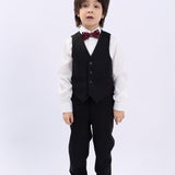 A young boy stands facing forward against a plain white background, wearing a white shirt, dark vest and pants, dress shoes, and the KIKI and JOJO Kids Bow Tie – Burgundy Bear – Pre-Tied Satin – Adjustable.