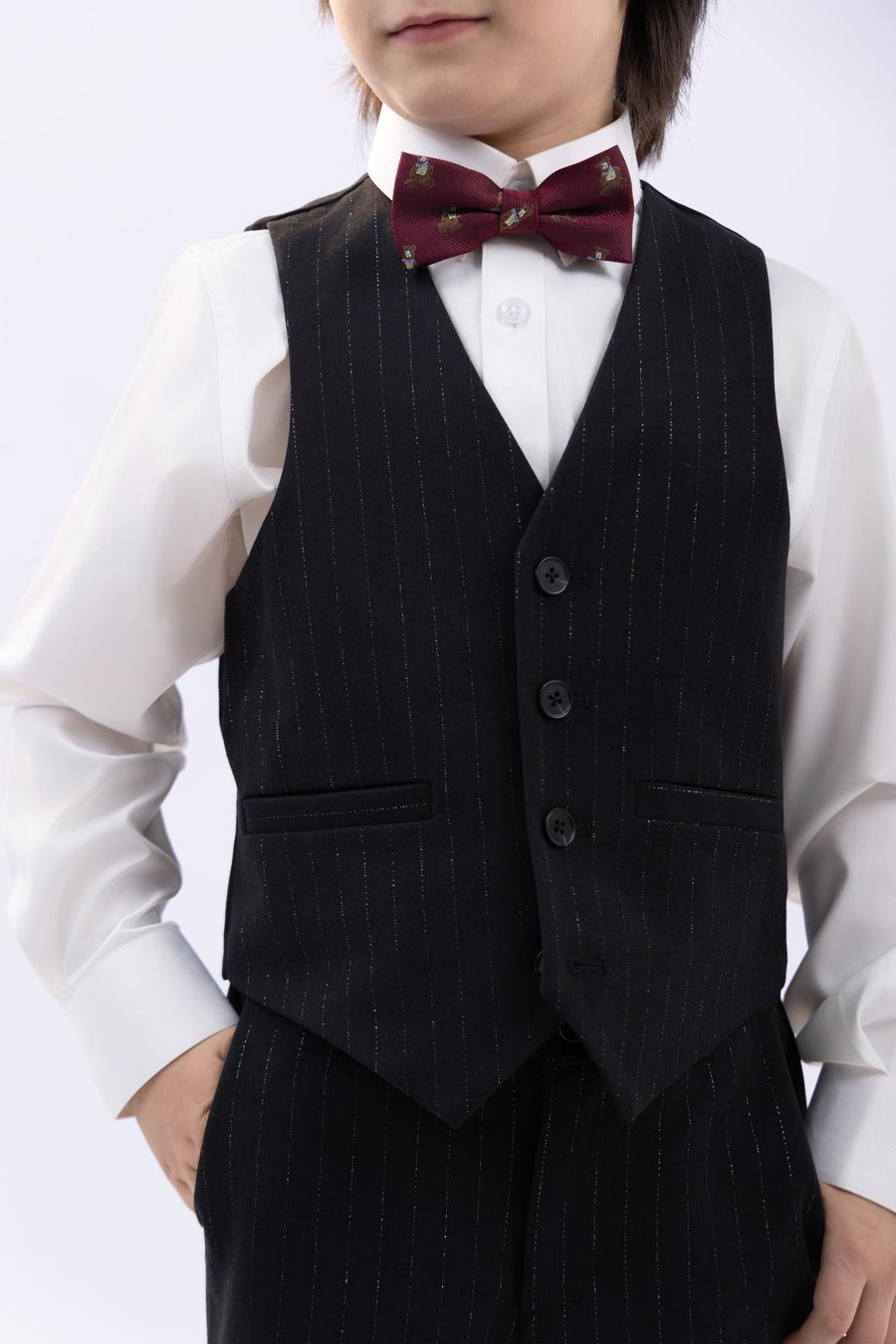 A young boy wears a white dress shirt, black pinstripe vest and pants, and a KIKI and JOJO Kids Bow Tie – Burgundy Bear – Pre-Tied Satin – Adjustable, with one hand in his pocket.